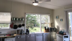 A kitchen with a ceiling fan, a window with a view of greenery, and various kitchen appliances.
