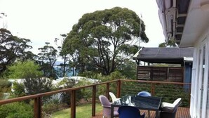 A wooden deck with a table and chairs, overlooking a garden and trees.