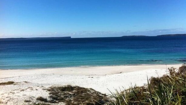 A beach with clear blue water and a sandy shore.
