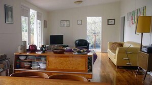 A living room with a TV, a sofa, a dining table with chairs, and a kitchen area with cabinets and a stove.