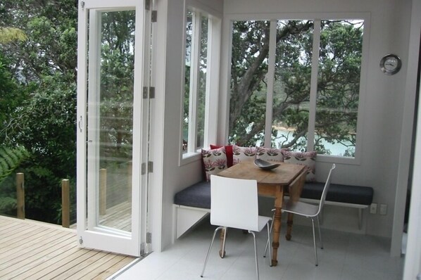 A room with a wooden table and white chairs, a bench with cushions, and a sliding glass door leading to a deck.