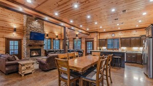 Un'ampia zona giorno con camino in pietra, soffitto in legno e tavolo da pranzo con sedie.