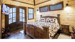 Camera da letto in una baita di legno, con un letto, una televisione e una porta con finestre.