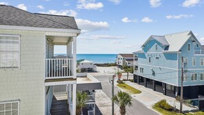 A coastal residential area with beachfront properties, including a two-story house with a balcony and a light blue building with a balcony.