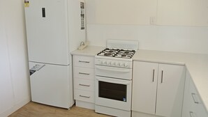Una cocina compacta con un refrigerador blanco, una estufa a gas, un microondas y un reloj en la pared.
