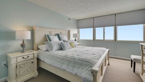 Ein Schlafzimmer mit einem Bett, Nachttischen, einer Lampe und einem Fenster mit Jalousien.