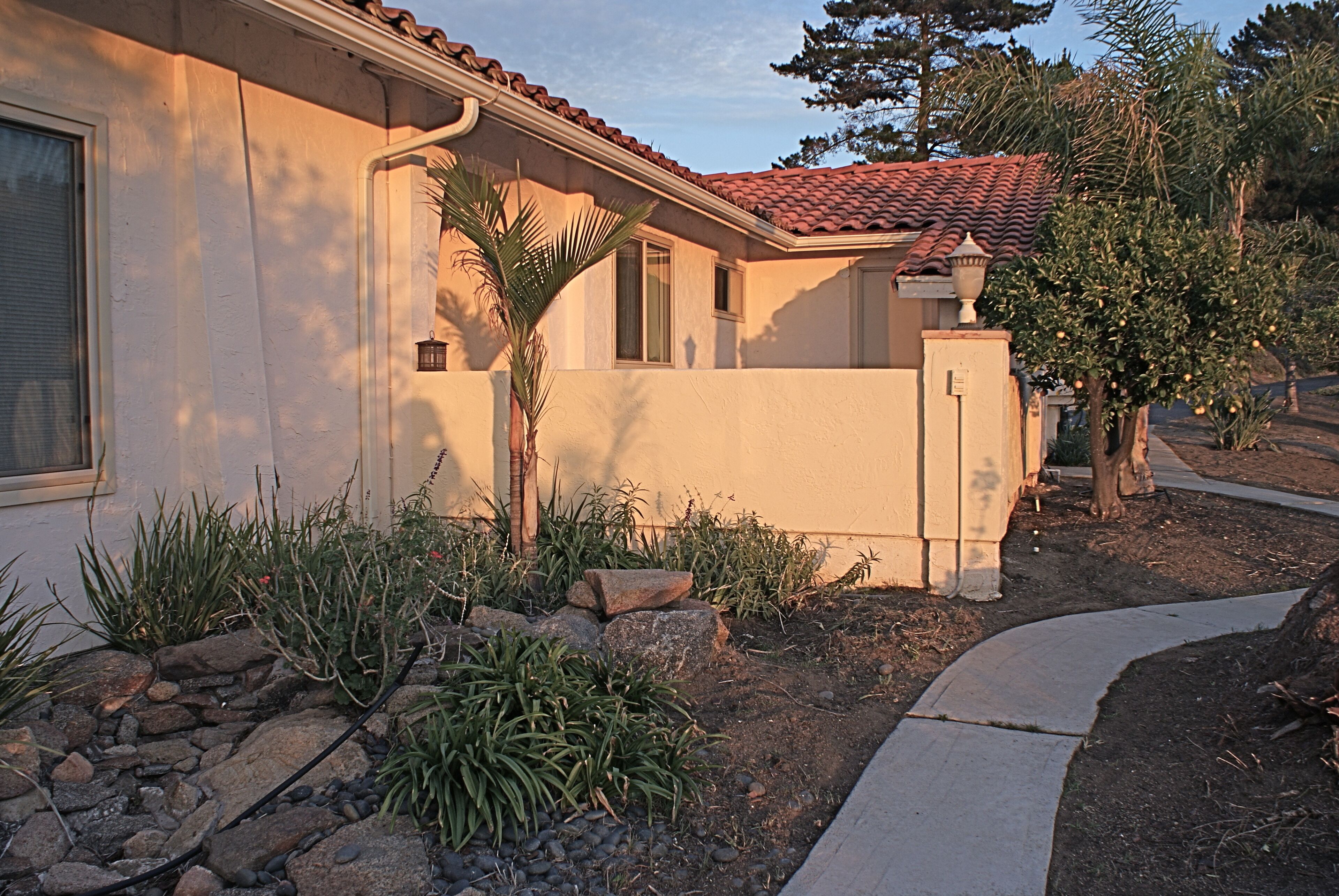 Une maison à l’extérieur beige, avec un toit en tuiles et un petit jardin agrémenté de rochers et de plantes.