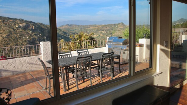 A balcony with a table and chairs, a grill, and a view of the hills. - Quiet Hilltop Home With Stunning Hill Top And Valley Views (Valley Center)