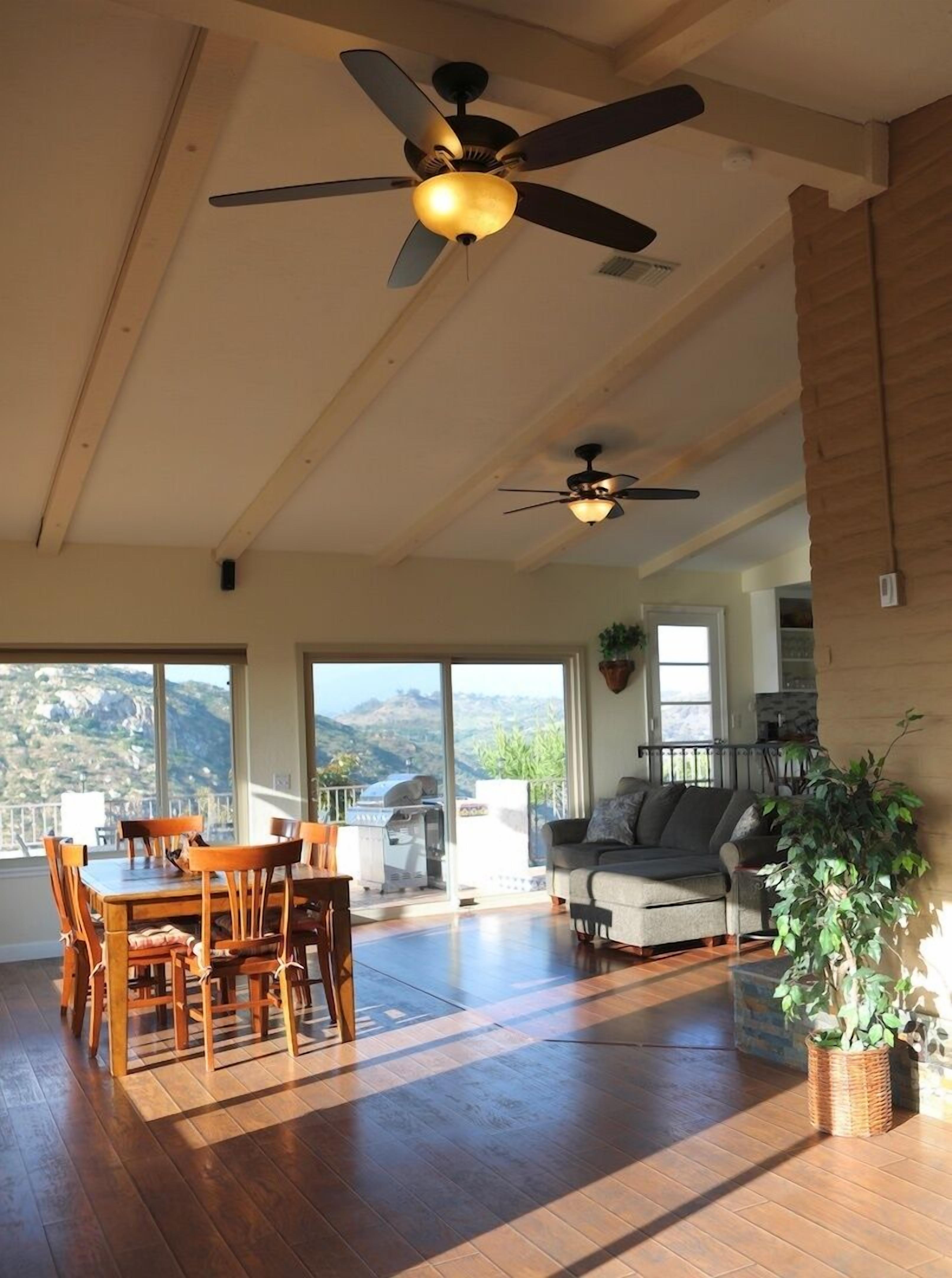 A spacious living area with a dining table and chairs, a sofa, and two ceiling fans.