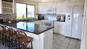 A modern kitchen with a large island, white cabinetry, a microwave, a refrigerator, and a window providing a view. - Quiet Hilltop Home With Stunning Hill Top And Valley Views (Valley Center)
