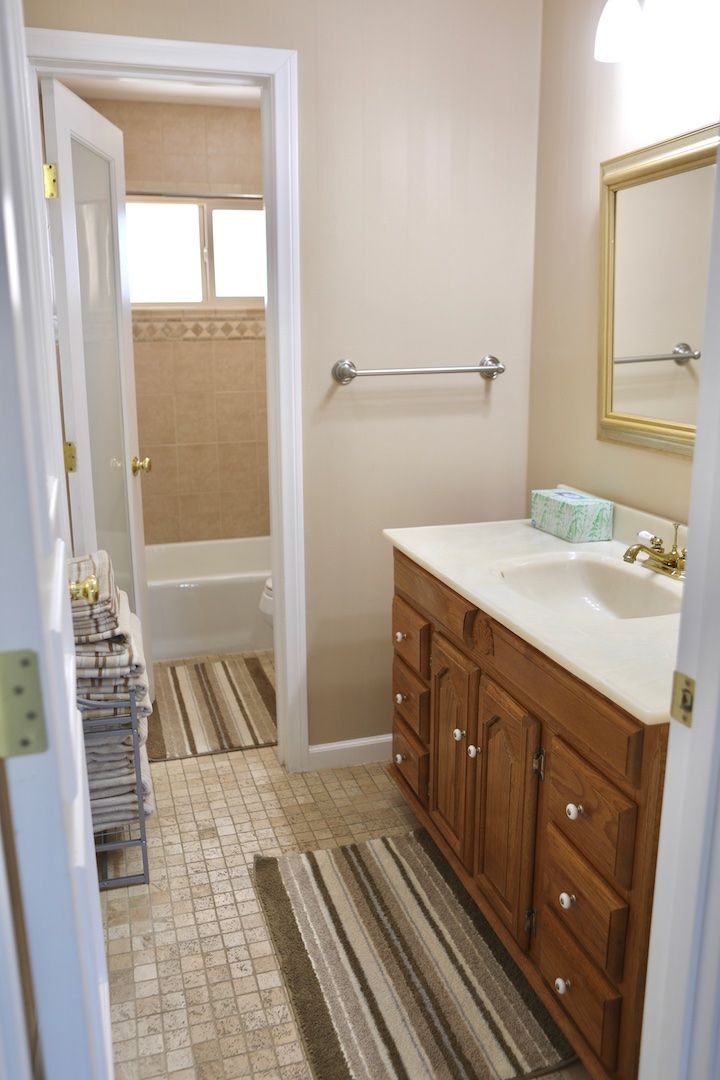 A bathroom with a bathtub, a sink, and a mirror. There is a towel rack with towels and a striped rug on the floor.