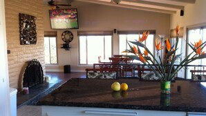 A spacious kitchen with a large island, a dining area with a wooden table and chairs, and a living area with a TV and decorative items. - Quiet Hilltop Home With Stunning Hill Top And Valley Views (Valley Center)