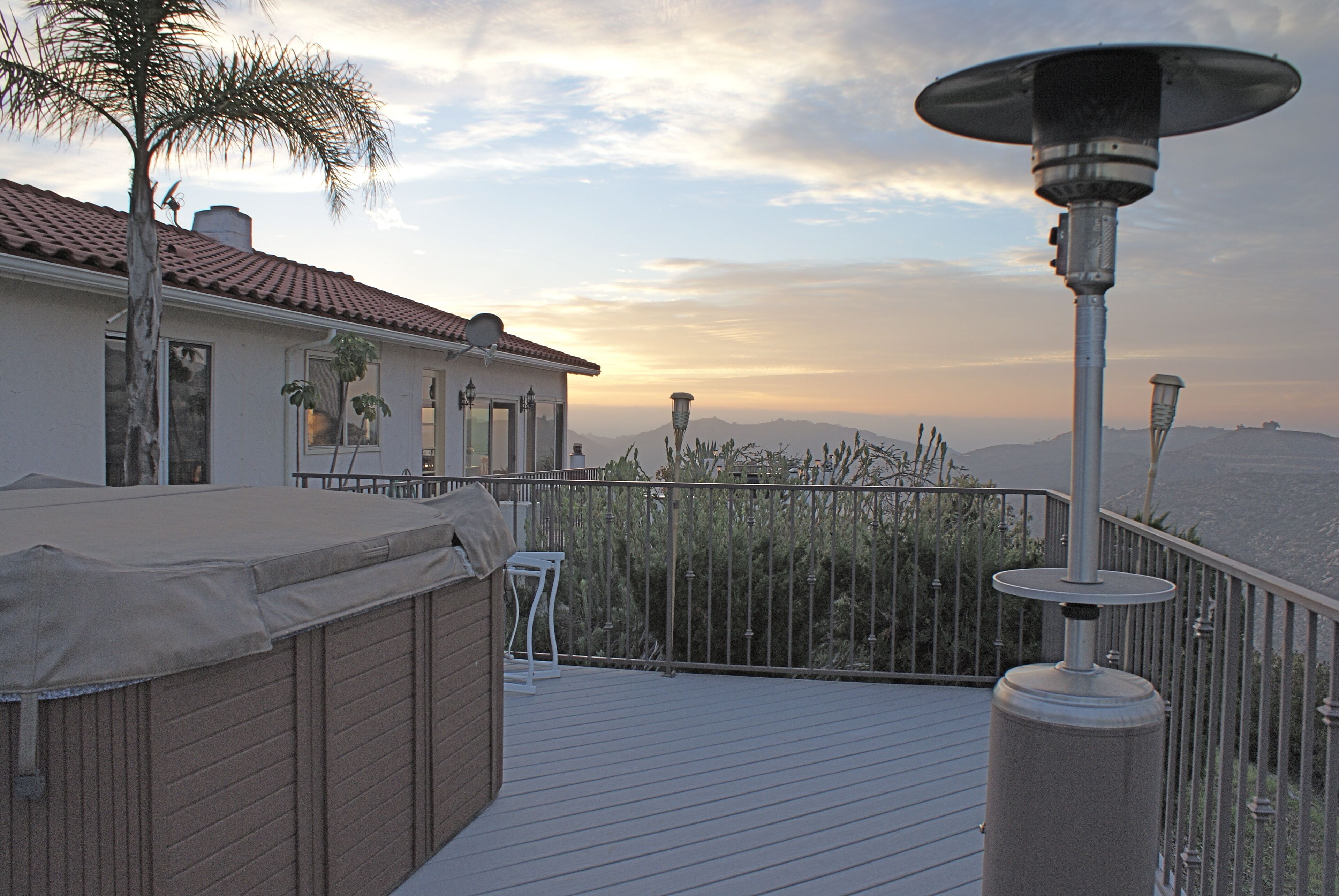 A deck with a hot tub, a covered seating area, and a view of the ocean at sunset.