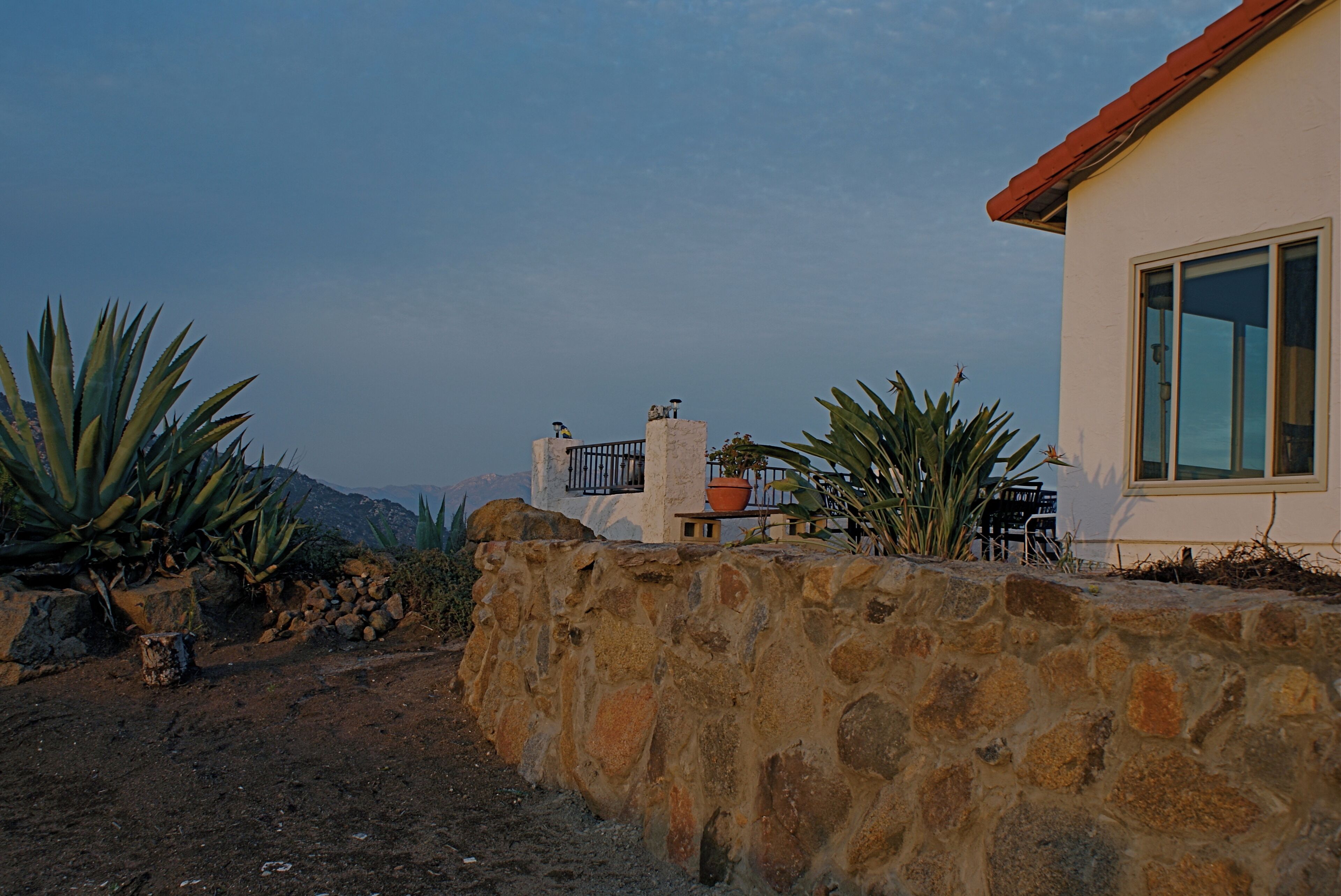A stone wall, a building with a red roof, and a mountain in the background.