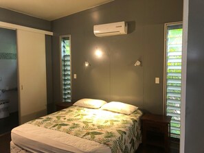 A bedroom with a bed, an air conditioner, a window with blinds, and a door leading to a bathroom. - Premier and Stunning Beach Front Location UNIT 4 (Nikao)