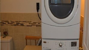 En kombinerad tvätt- och torkmaskin, placerad ovanpå varandra, i ett badrum med kaklade väggar och en liten bänk.