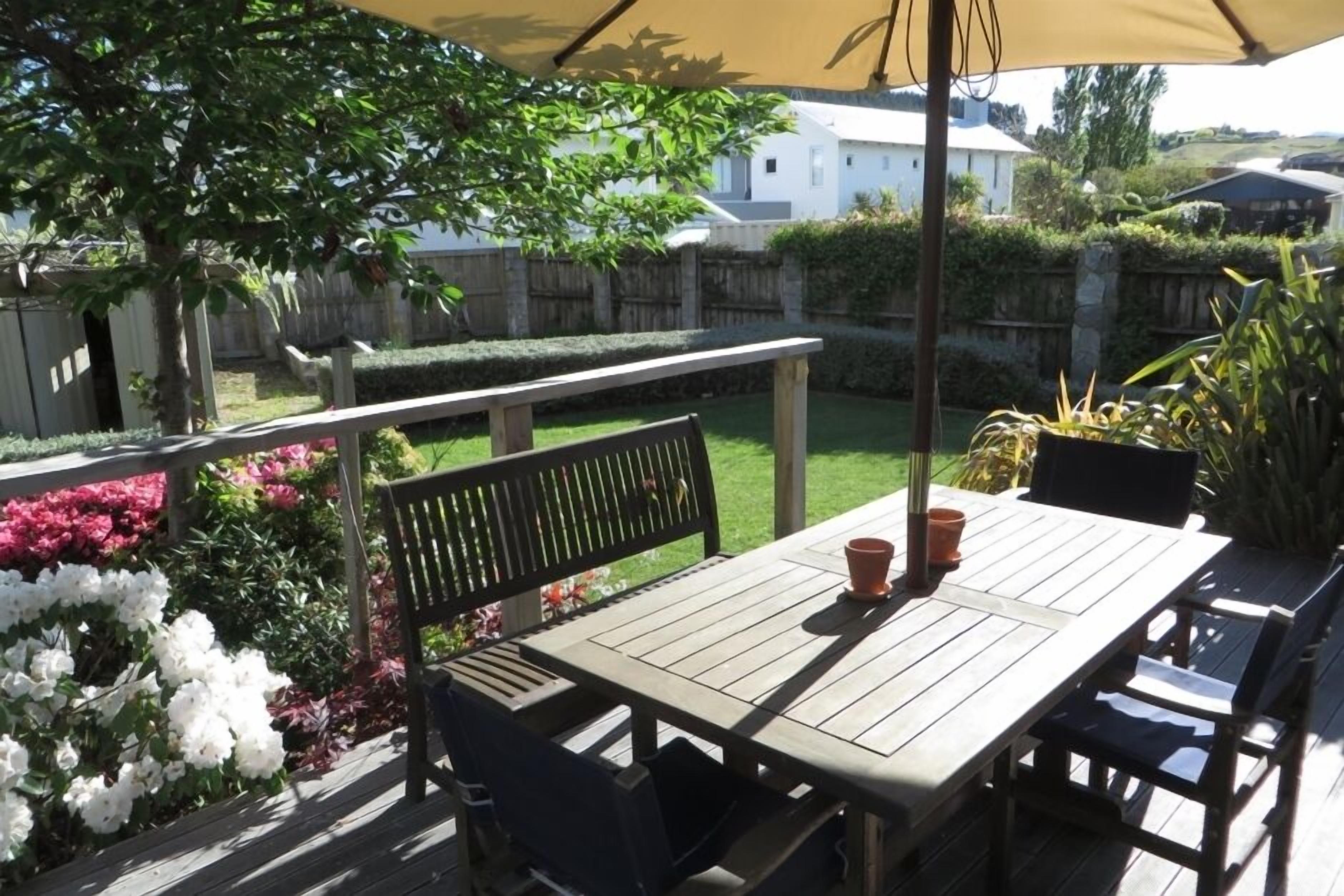 A wooden deck with a table and chairs, surrounded by a garden with various plants and flowers.
