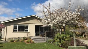 A two-story house with a front porch, a small garden, and a tree with white blossoms. -  Located near Eely Point  (Wanaka)