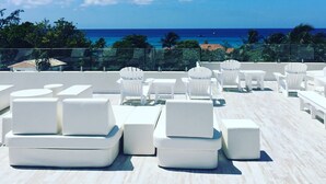 Une terrasse sur le toit, dotée de mobilier d’extérieur blanc, offrant une vue dégagée sur l’océan et une vue lointaine sur le paysage urbain.