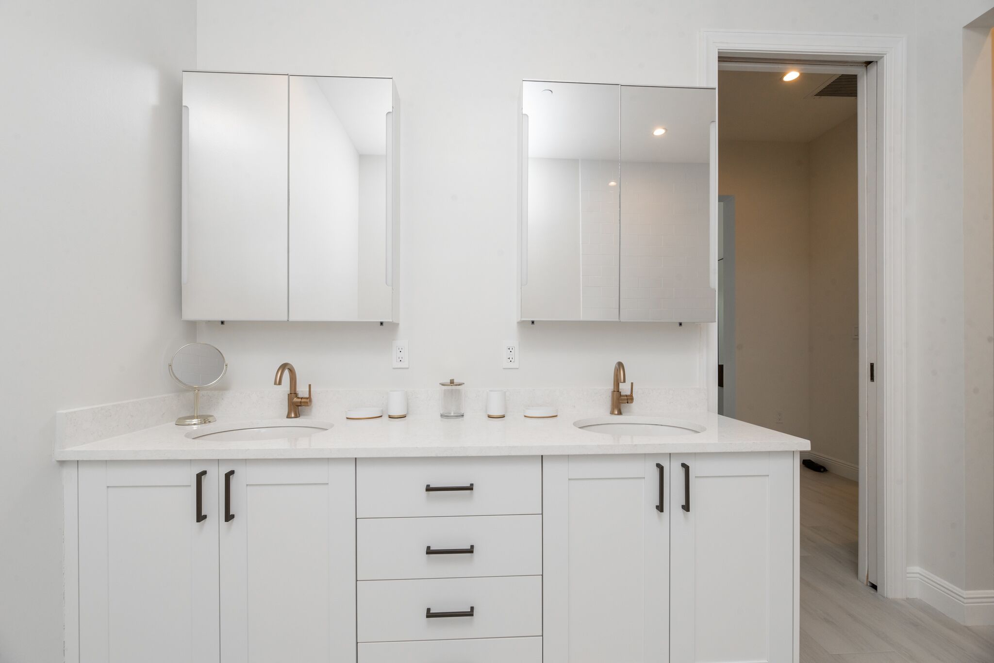 A modern bathroom with white cabinetry, two sinks, and a large mirror above each sink.