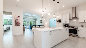 Une cuisine moderne avec des meubles blancs, des appareils en acier inoxydable et des luminaires suspendus.