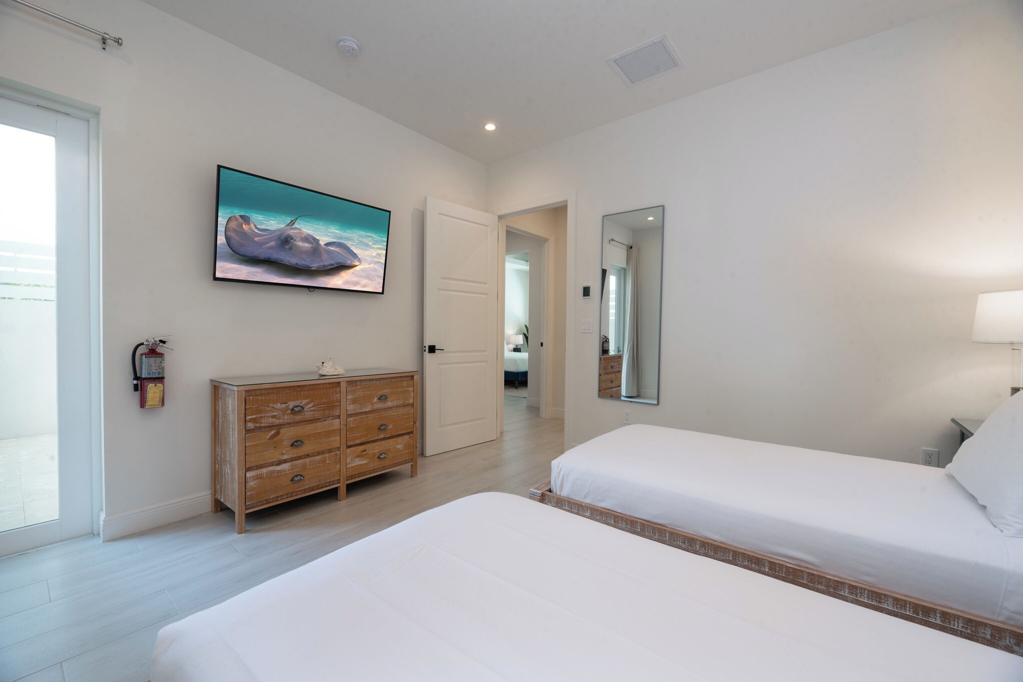 A bedroom with two beds, a wooden dresser, a painting on the wall, and a door leading to another room.