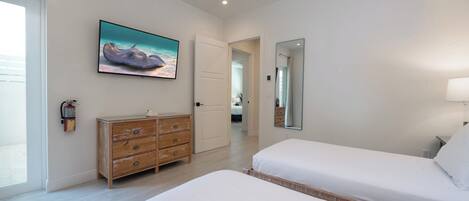 A bedroom with two beds, a wooden dresser, a painting on the wall, and a door leading to another room.