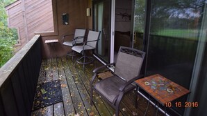 A covered outdoor area with a wooden deck, two chairs, a small table, and a sliding glass door leading to a room. - No Worries at Summit Village! (bellaire)