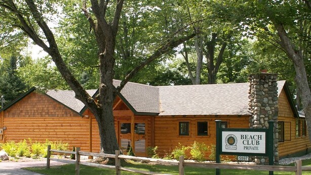 A wooden cabin with a stone chimney, surrounded by trees, labeled as a private beach club. - No Worries at Summit Village! (bellaire)