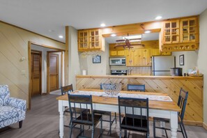 A dining area with a wooden table and chairs, a kitchen with wooden cabinets and appliances, and a patterned armchair. - No Worries at Summit Village! (bellaire)