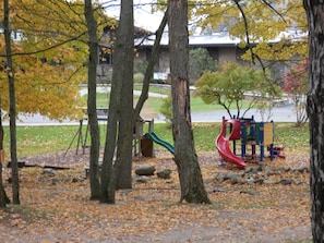 A park with playground equipment, trees, and a building in the background.