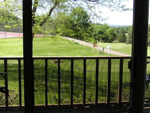 A view from a porch overlooking a well-maintained lawn with a pathway and a sports field in the background.