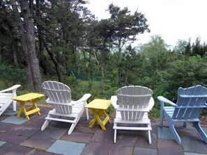 A patio with Adirondack chairs and small tables, surrounded by trees.