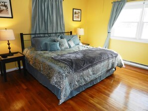 A bedroom with a bed, two bedside tables, a window with curtains, and a wall with a picture. - Serene Escape in South Rehoboth - Private Pool + Pet-Friendly (Rehoboth Beach)