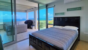 Ein Schlafzimmer mit einem großen Bett, Meerblick und einer Schiebetür zu einer Sitzgelegenheit im Freien.