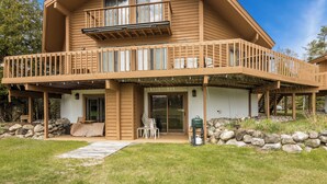 A two-story wooden house with a balcony, a covered patio, and a stone wall. - Playing Hookie at Schuss (mancelona)