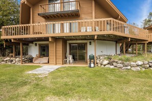 A two-story wooden house with a balcony, a covered patio, and a stone wall. - Playing Hookie at Schuss (mancelona)