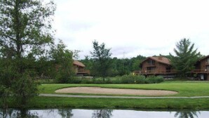 A lakeside view of a lodge with two wooden cabins, a grassy area, and a pond. - Playing Hookie at Schuss (mancelona)