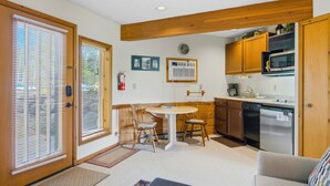 A compact kitchen with wooden cabinets, a microwave, and a dishwasher. There is a dining area with a table and chairs. - Playing Hookie at Schuss (mancelona)