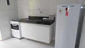Una cocina compacta con armarios blancos, una encimera negra, un refrigerador blanco y una estufa.