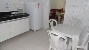 Una pequeña cocina con armarios blancos, un refrigerador blanco, una encimera negra y una mesa de comedor con sillas blancas.