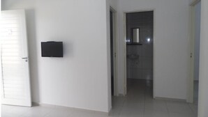 Un pasillo con una puerta blanca a la izquierda, un objeto negro en la pared y un baño visible a través de la puerta.