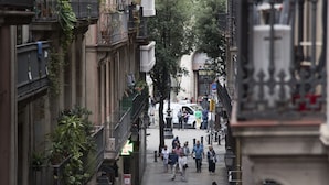 Eine schmale Stadtstraße gesäumt von mehrstöckigen Gebäuden, einige mit Balkonen und Pflanzen.