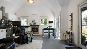 A modern living room with a fireplace, a dining area, and a kitchen with black tiled backsplash. - Cottage 4A- sweet retreat with spa in Daylesford (Daylesford)