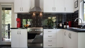 A modern kitchen with white cabinets, a black tiled backsplash, stainless steel appliances, and a red coffee maker. - Cottage 4A- sweet retreat with spa in Daylesford (Daylesford)