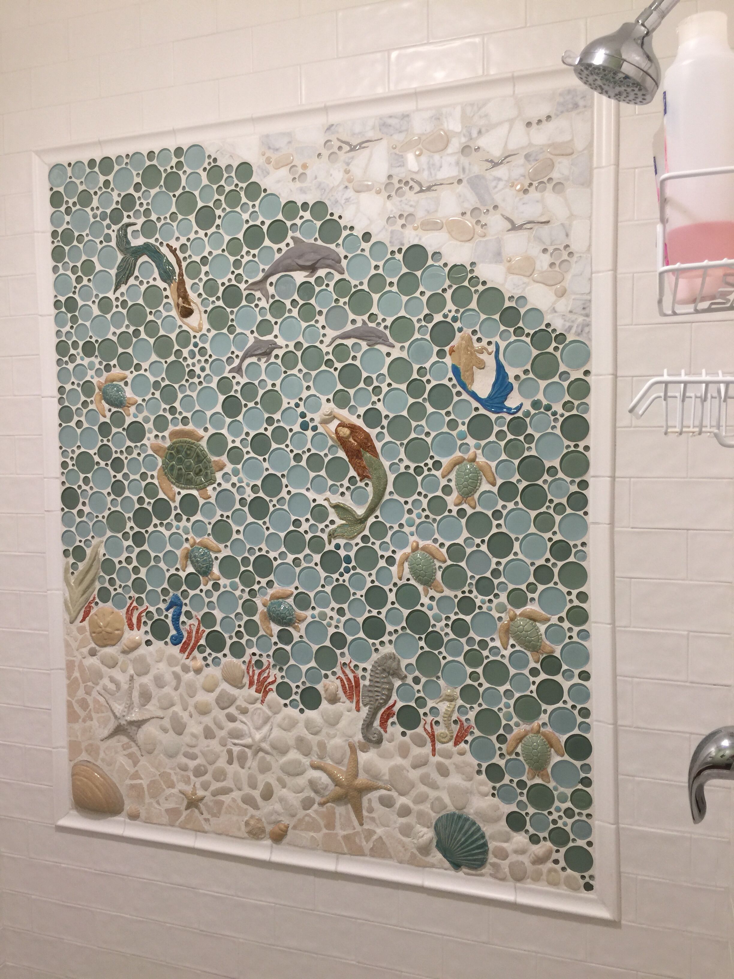 Een badkamer met een mozaïekwand waarop zeedieren en schelpen afgebeeld zijn.