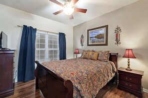 A bedroom with a bed, a ceiling fan, a window with curtains, a bedside table with a lamp, and a wall-mounted picture. - Pool&SplashPad&PlayGround OutTheBackDoor - LakeView-PoolTable-FoosBall++ (Hollister)