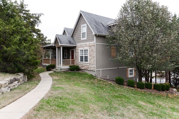A two-story house with a stone facade, a covered porch, and a well-maintained lawn. - Pool&SplashPad&PlayGround OutTheBackDoor - LakeView-PoolTable-FoosBall++ (Hollister)
