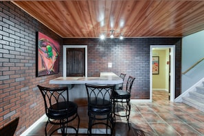 Cozy dining area with a long table and four chairs, surrounded by a brick-patterned wall and a framed artwork.