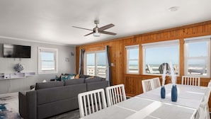 A living room with a sofa, dining table, chairs, a ceiling fan, and a TV. - 600 Nags Head Ocean-Front Completely Renovated (Nags Head)